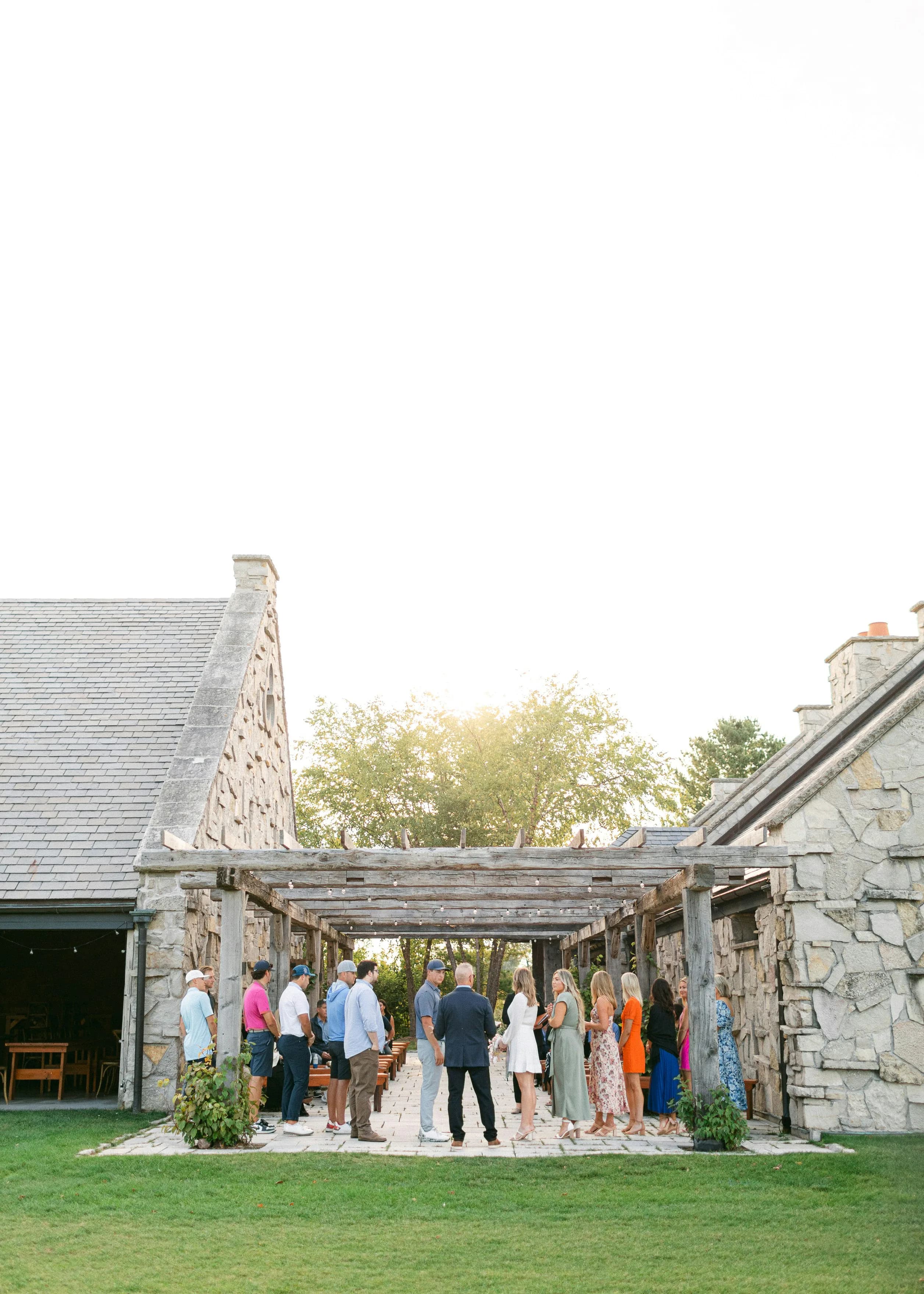 Invitados reunidos bajo una pérgola con guirnaldas de luces al atardecer