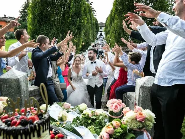 Newlyweds walking through a crowd of cheering guests, with the cake and flowers in the foreground