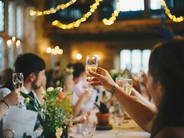 Guests raising glasses of sparkling wine at a long table under string lights